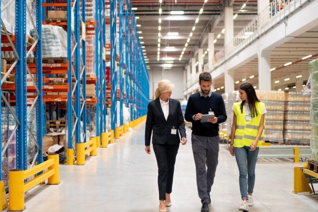 Drei Logistikmitarbeiter gehen durch ein Lager und nutzen mobile Datenerfassung per Tablet zur Bestandsprüfung.