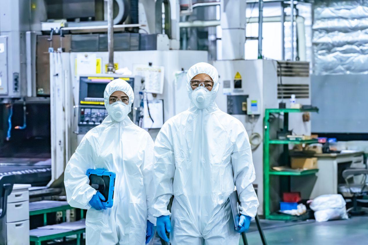 Zwei Reinraumreinigung-Fachkraefte in voller Schutzkleidung stehen in einer Industriehalle