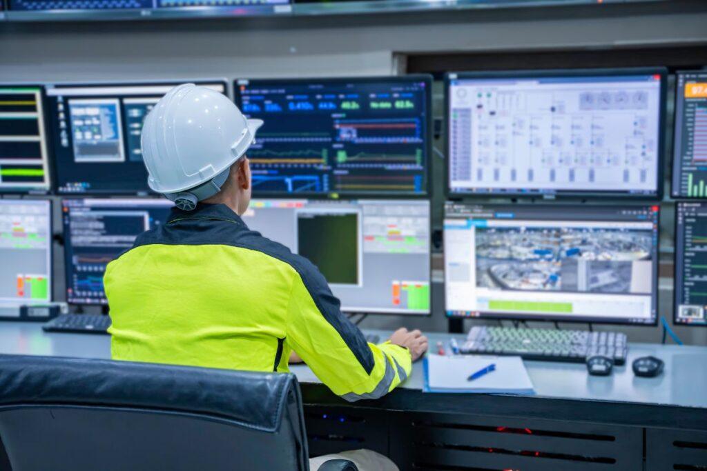 Industriearbeiter mit Helm vor Kontrollsystem zur Ueberwachung von Lastaufnahmemitteln und smarten Anlagen