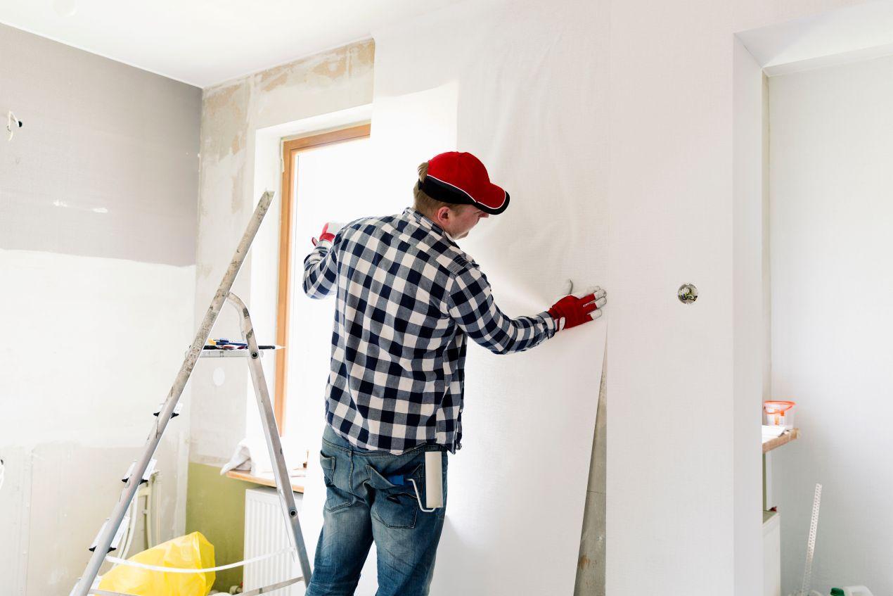 wohnungssanierung berlin: Handwerker bringt neue Tapete in renovierungsbedürftiger Wohnung fachgerecht an