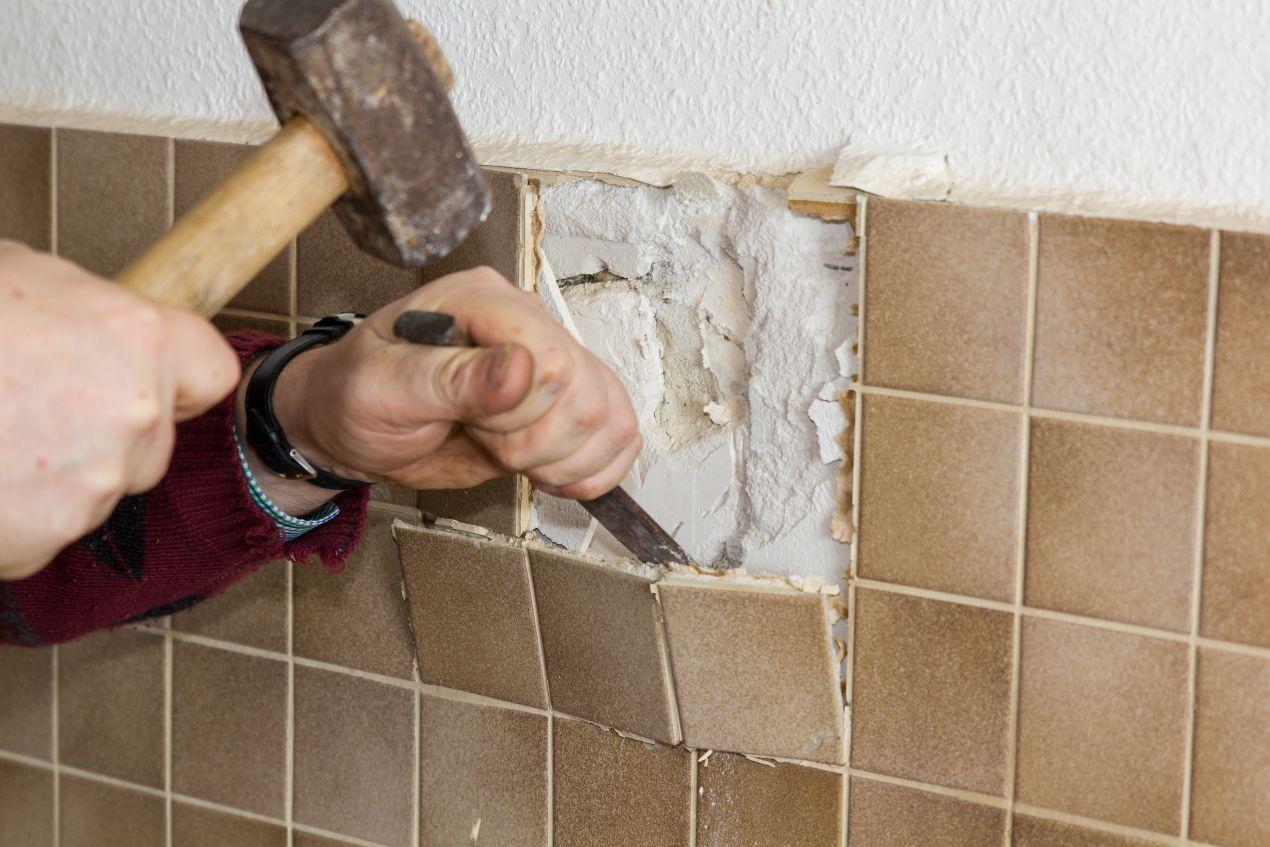 wohnungssanierung berlin: Nahaufnahme von Handwerker bei der Entfernung alter Badezimmerfliesen mit Hammer und Meißel